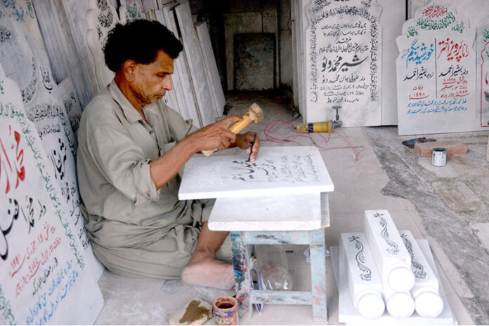 A skilled worker carves intricate names into a piece of marble at his workplace