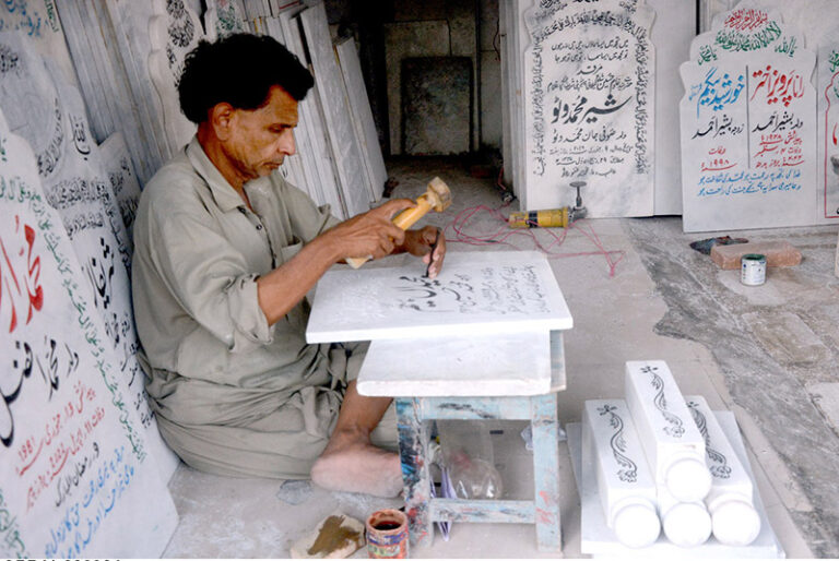 A skilled worker carves intricate names into a piece of marble at his