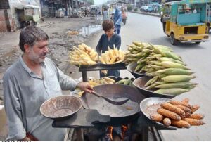 A vendor busy in roasting corn cobs to attract customers at his roadside setup.