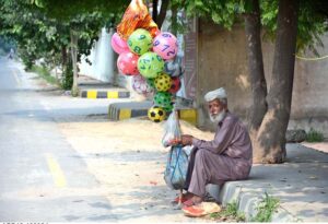 A street vendor holds colorful balloons, waits patiently and hoping to attract passersby and earn a livelihood for his family, at roadside in the city.