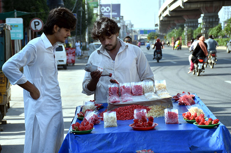A vendor sells fresh pomegranates at the roadside, attracting customers