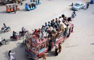 An overloaded bus with men precariously perched on its roof maneuvers through the busy streets of Korangi, posing a serious risk of a potential mishap in the city.