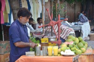 A vendor prepares fresh grape juice at his roadside stand, attracting the attention of passers-by.