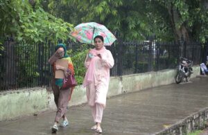 A woman shelters under an umbrella as she walks through the rain in front of Company Bagh in the city.