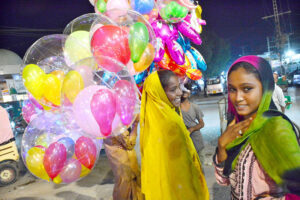 Street vendor girls carry brightly illuminated balloons to sell and attract the customers in Latifabad.