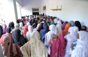 Women wait patiently on the ground without proper seating for their turn to receive their quarterly installment at the Benazir Income Support Program payment distribution center in Company Bagh.