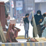 An elderly woman vendor selling brooms while sitting at footpath to earn livelihood
