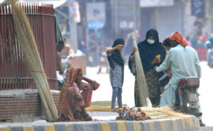 An elderly woman vendor selling brooms while sitting at footpath to earn livelihood