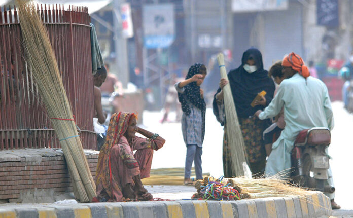 An elderly woman vendor selling brooms while sitting at footpath to earn livelihood