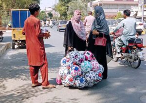 Women are purchasing footballs from a street vendor along the roadside in the city .