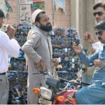 A motorcyclist selecting and purchasing sunglasses from a roadside vendor