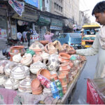 A man carefully selecting handmade pottery from a display on a handcart at sheen chowk