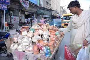 A man carefully selecting handmade pottery from a display on a handcart at sheen chowk