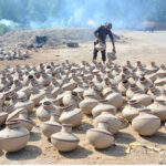 A worker placing clay pitchers under sunlight to dry at Kumhar Para