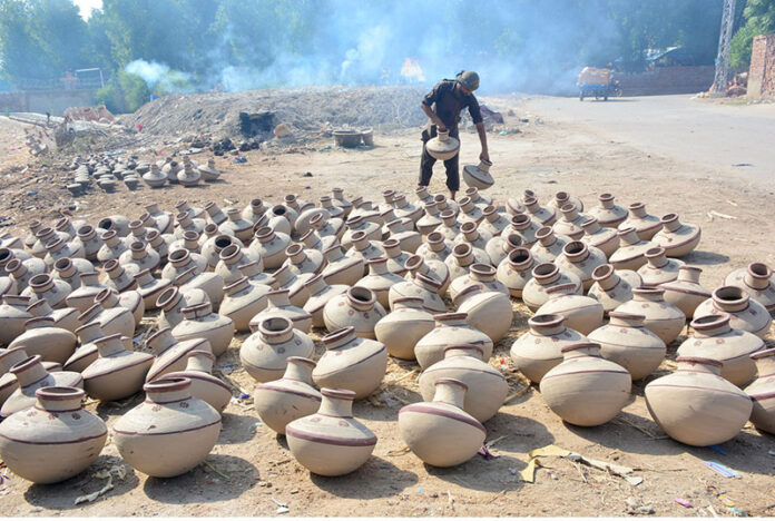 A worker placing clay pitchers under sunlight to dry at Kumhar Para