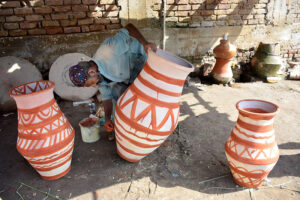 A worker placing clay pitchers under sunlight to dry at Kumhar Para