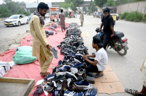 Youngsters selecting and purchasing local made shoes from a roadside vendor in the city.