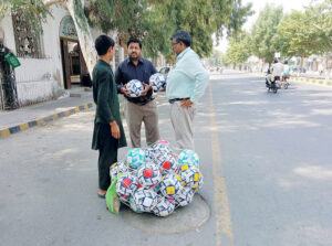 People purchase footballs from a young vendor at the roadside.