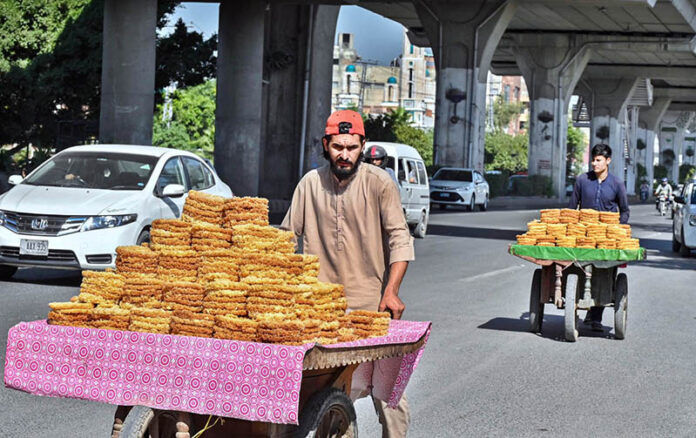 Street vendors push their handcarts with sweets items on the busy Murree Road, seeking customers amidst the lively crowd