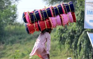 A street vendor balancing sitting stools on his head while making his way through Karal Chowk in search of customers in Federal Capital.