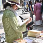 A woman busy in selecting and purchasing old books from roadside stall at Mall Road