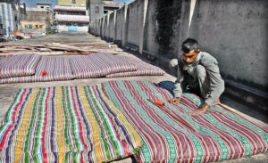 A worker busy in stitching a quilt at his workshop in preparation for the upcoming winter season