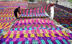 Workers spread traditional colorful clothe sheets under the sun for drying purpose at Tando Agha area.
