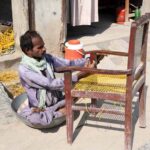 A disabled person is busy repairing a chair in front of his shop near Bakapur Village
