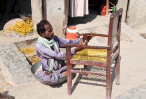 A disabled person is busy repairing a chair in front of his shop near Bakapur Village