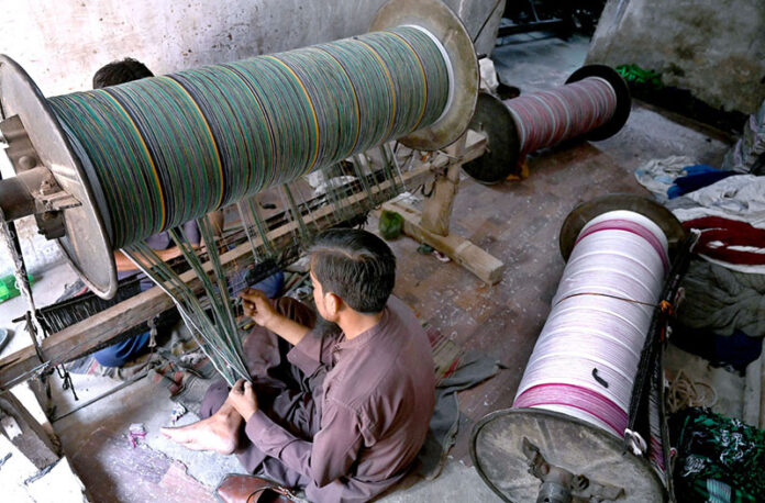 Workers busy in preparing and arranging thread for preparing fabric by machine at a local textile factory