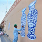 An artist is busy giving the final touch on the painting on the wall of the flyover