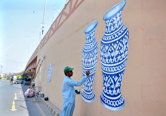 An artist is busy giving the final touch on the painting on the wall of the flyover