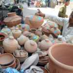 A young vendor showcases an array of colorful clay pots, hoping to attract buyers with their traditional charm