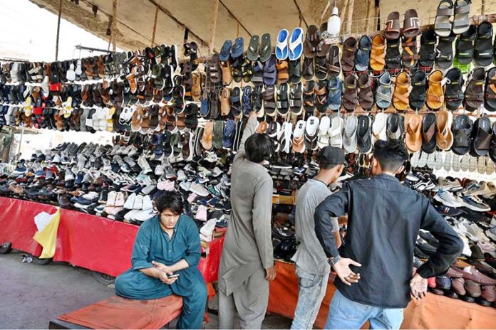 People selecting and purchasing shoes from setup under the shade of Makki Shah Flyover