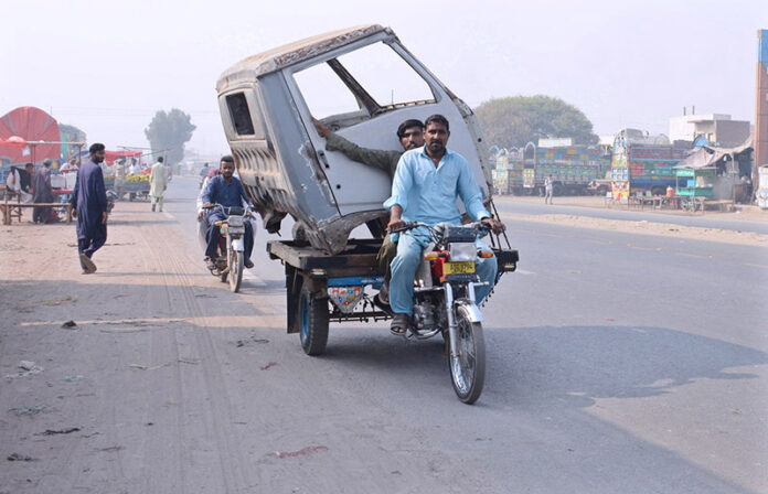 A tricycle rider transports the front body of a mini truck to a workshop, navigating with an unusual load in the city streets