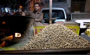A hawker roasts fresh peanuts at his stall, a popular winter treat in high demand for its seasonal warmth and rich flavor