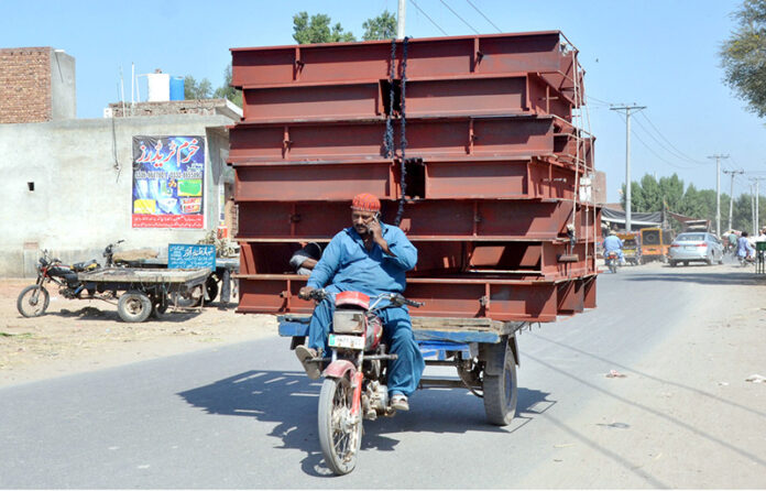 A tricycle holder on the way loaded with door frames while busy in the cell phone may cause any mishap