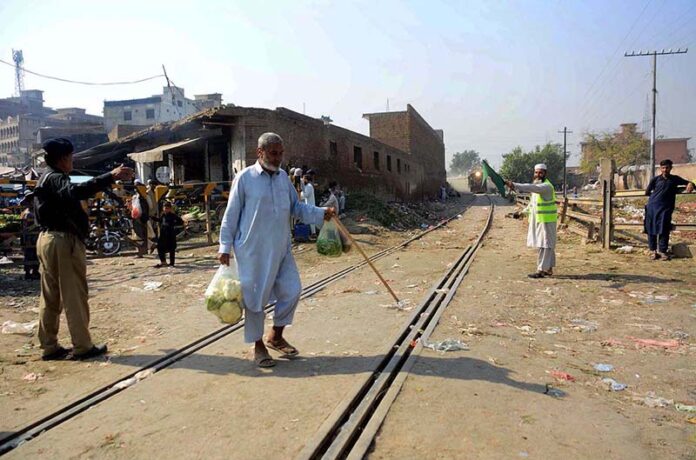 An old man is crossing a railway track while a train approaching may cause any mishap and needs the attention of concerned authorities near Sabzi Mandi