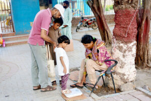 A caring parent weighs their daughter on a scale at a local park.