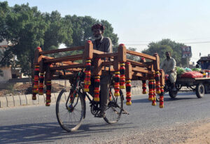 A cyclist on the way while loaded with frames of traditional bed heading towards the market.