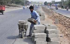 A laborer loading cement blocks onto a handcart during the diversion and expansion work at Head Muhammad Wala Road in the city.