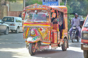 A beautifully decorated rickshaw adorned with traditional truck art moves with passengers along Radio Pakistan Road, adding color to the city’s daily life.