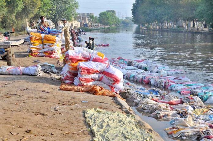 A large number of labourers are busy washing empty plastic bags in the canal