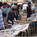 People selecting and purchasing old books from a roadside stall at Mall Road