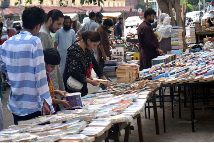 People selecting and purchasing old books from a roadside stall at Mall Road