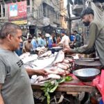 A vendor sells fish to attract customers outside his shop in a local market