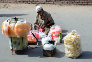 An elderly vendor sells snacks and crackers roadside to earn a livelihood in the city
