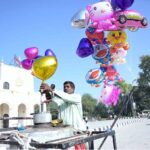 A street vendor fills gas into colorful balloons to attract children at GPO Chowk