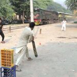 Youngsters enjoy a game of cricket near the railway track at Tewana Park, with a train approaching in the background