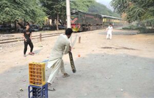 Youngsters enjoy a game of cricket near the railway track at Tewana Park, with a train approaching in the background